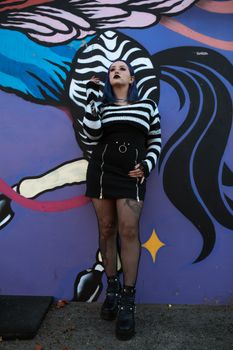 A stylish woman poses in front of colorful graffiti, showcasing street fashion.