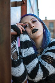 Portrait of a young adult showcasing edgy street fashion with vibrant hair and makeup.