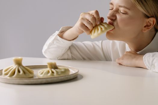 Young woman savoring traditional Georgian khinkali dumplings indoors at lunch.
