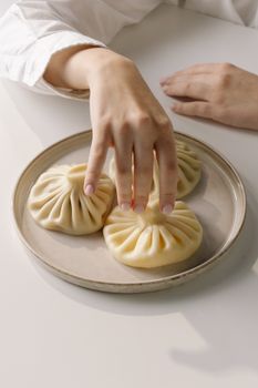 A person's hand holding raw dumplings on a plate, ready for cooking.