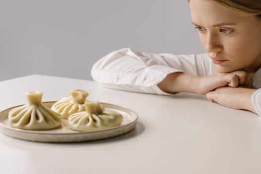 A woman in a white shirt gazes at a plate of traditional Georgian khinkali dumplings.