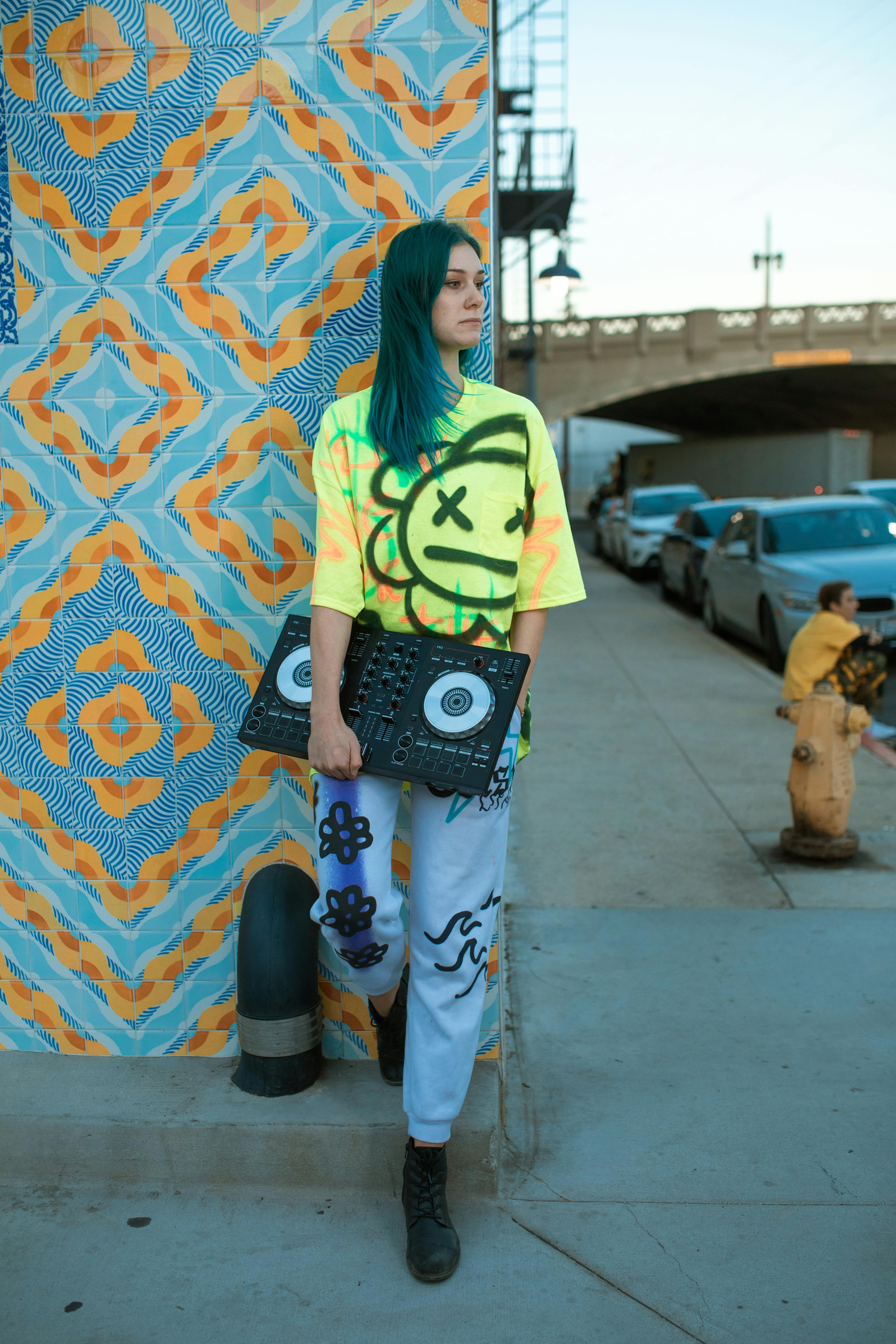 woman in green and white long sleeve shirt and blue denim jeans standing beside wall with during