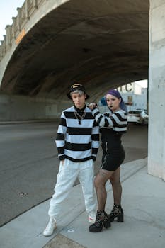 Two stylish Gen Z individuals in street fashion under an urban bridge.