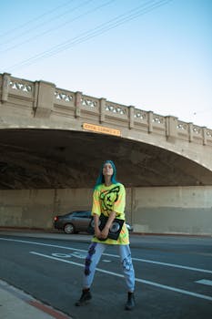 Teen skater in vibrant urban fashion posing under a classic bridge.