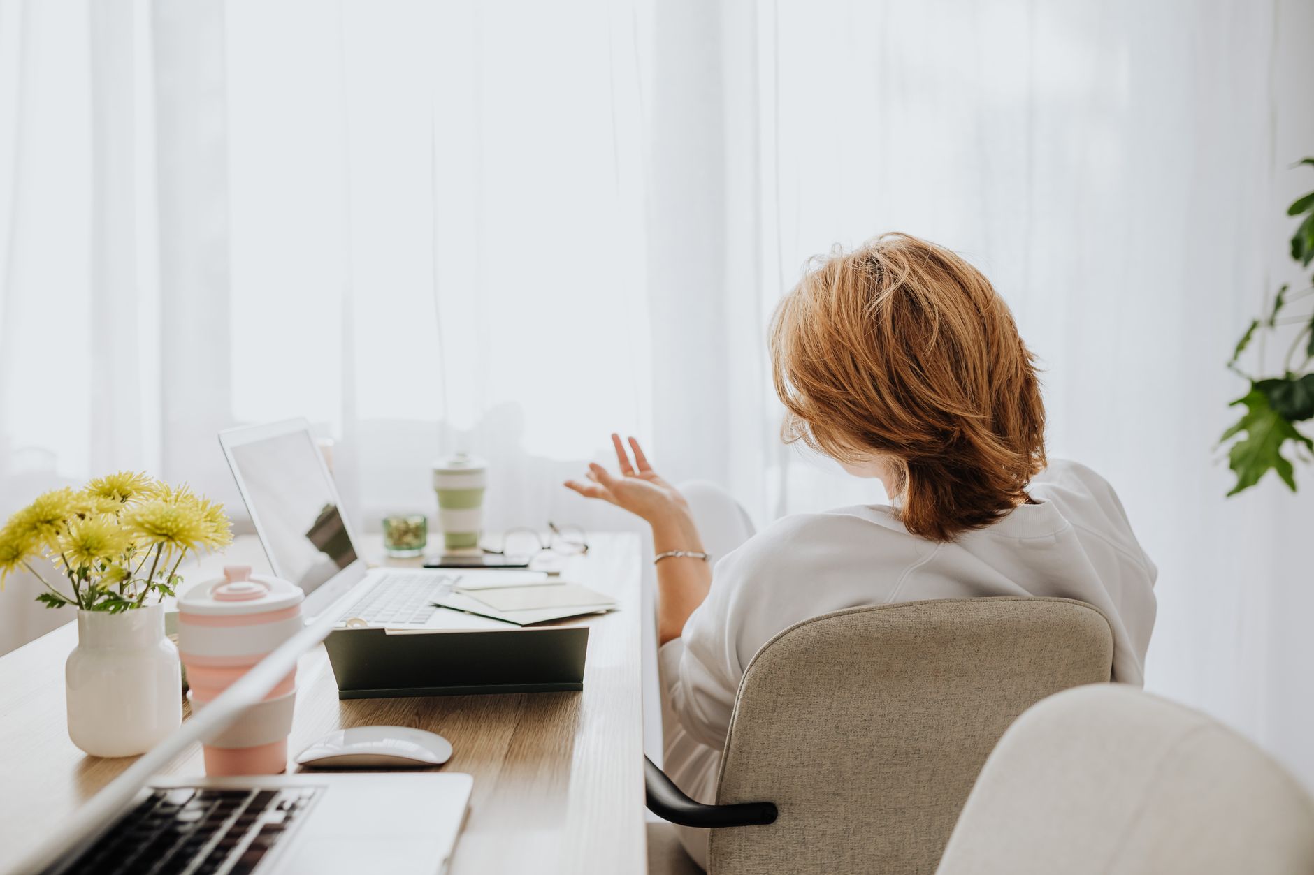 A coach on a video call at her desk, the laptop open in front of her in a bright room