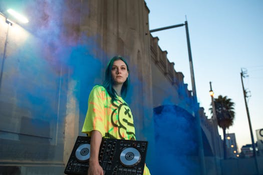 A young DJ in vibrant neon fashion stands outdoors with colorful smoke, setting a dynamic urban vibe.