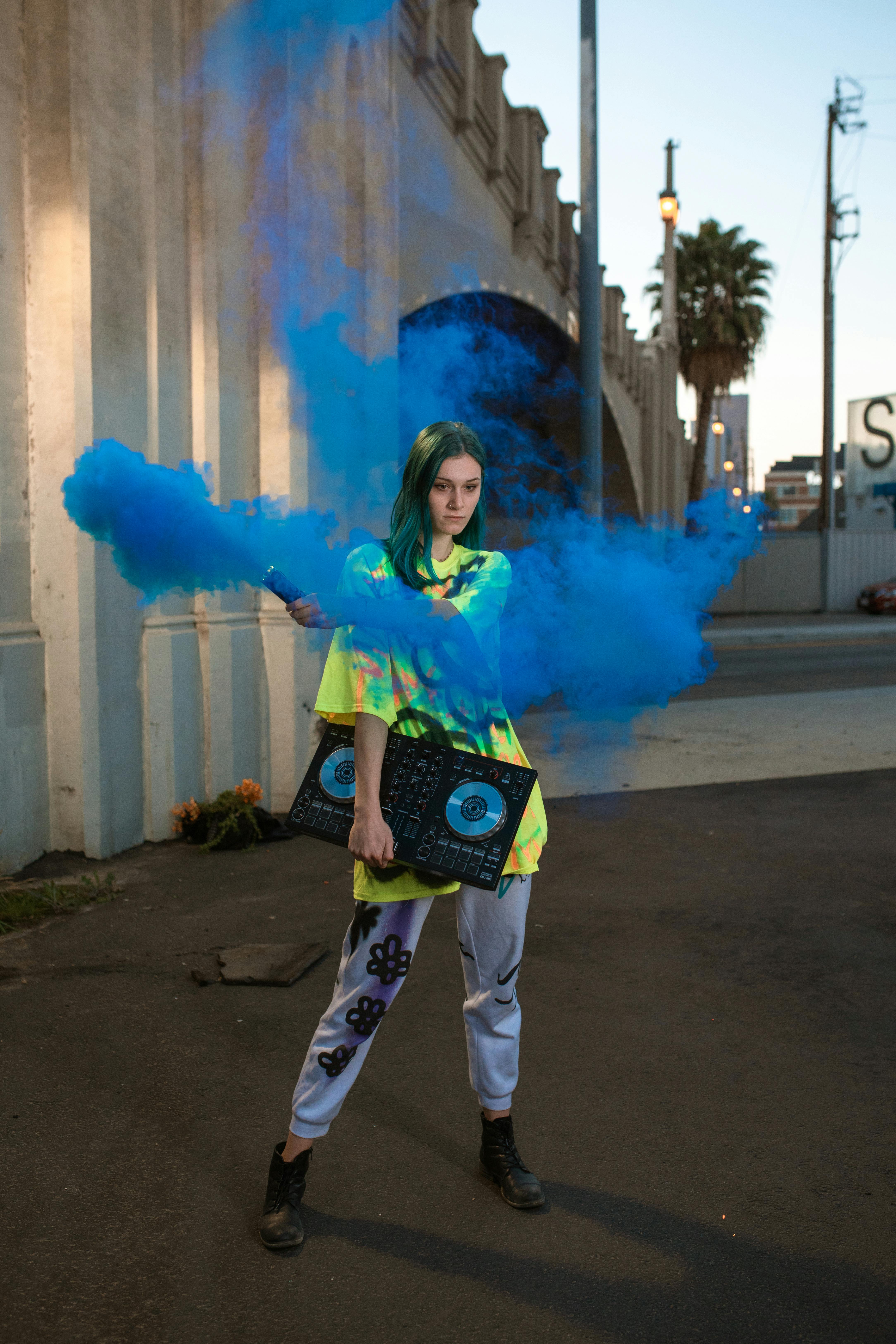 woman in green jacket and blue denim jeans holding green smoke