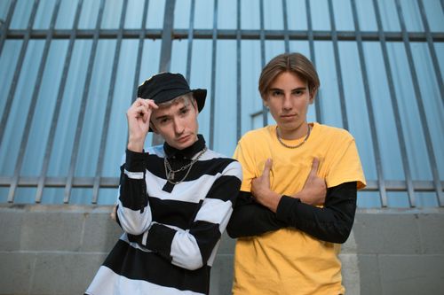 Free Two trendy teenagers posing in casual outfits against a metal fence background. Stock Photo