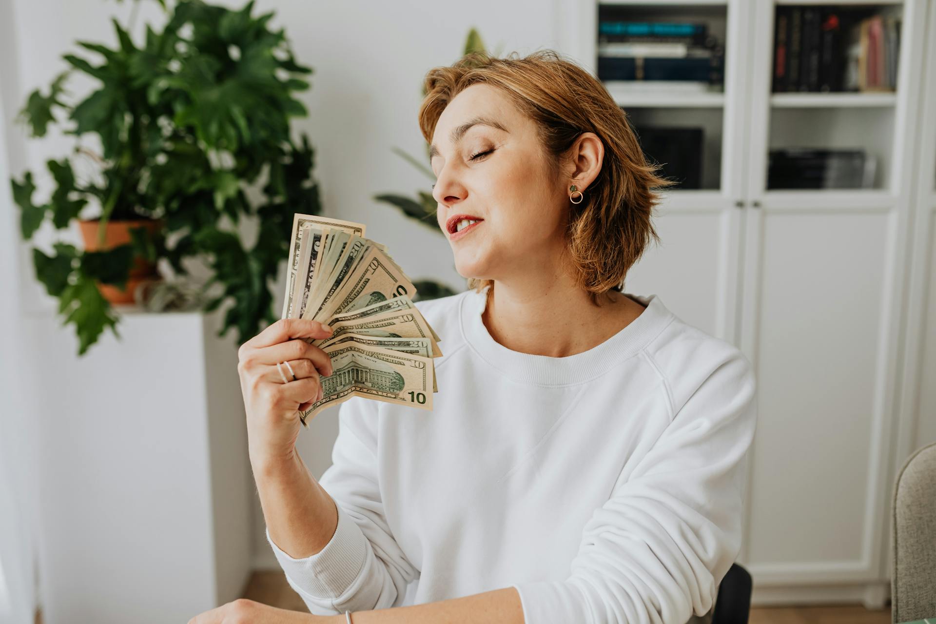 Woman holding US dollars in a relaxed indoor setting, reflecting satisfaction and success.