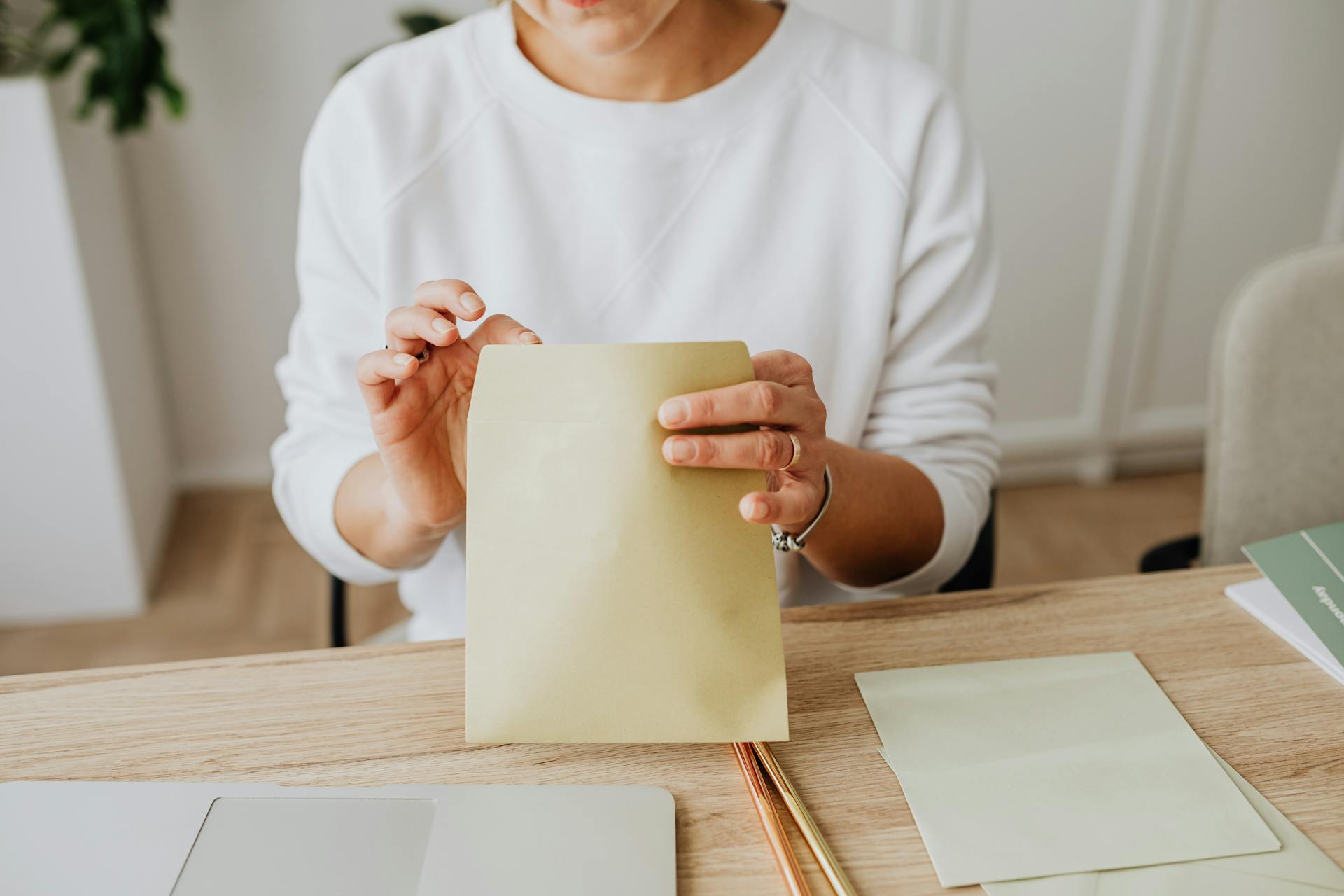 Close-up of a woman sealing a brown envelope while seated at a wooden desk indoors.