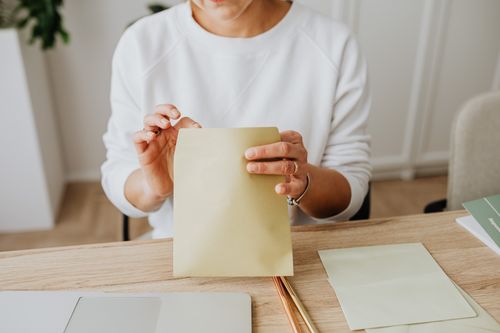 Free Close-up of a woman sealing a brown envelope while seated at a wooden desk indoors. Stock Photo
