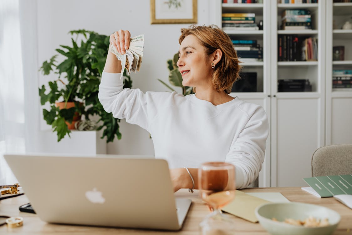 Woman Using Laptop While Holding Money