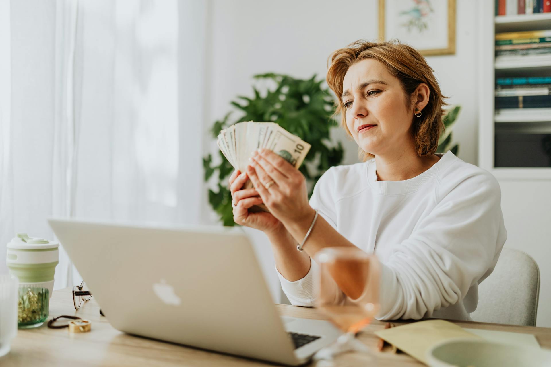 Woman counting money at her desk with a laptop, depicting financial management and success.