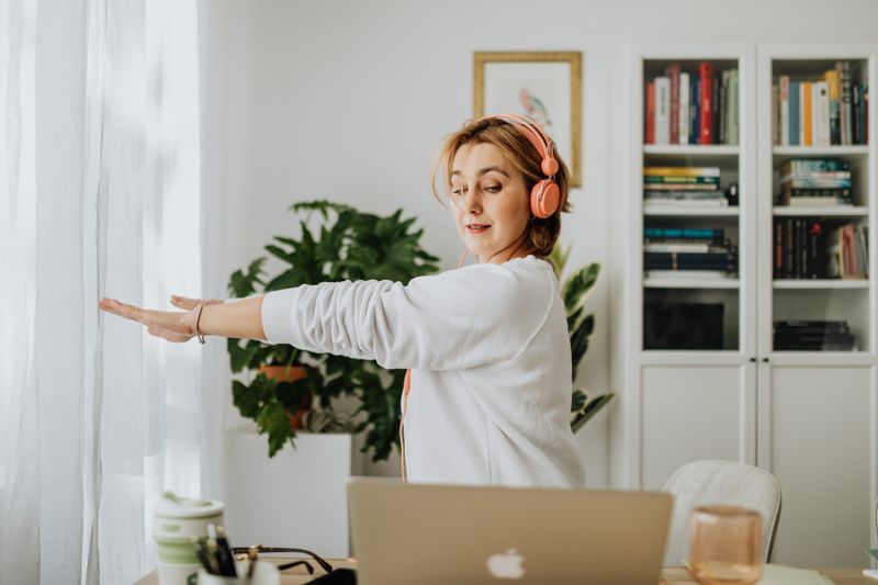 Person stretching at a home-office desk beside a laptop, photo by Kaboompics on Pexels