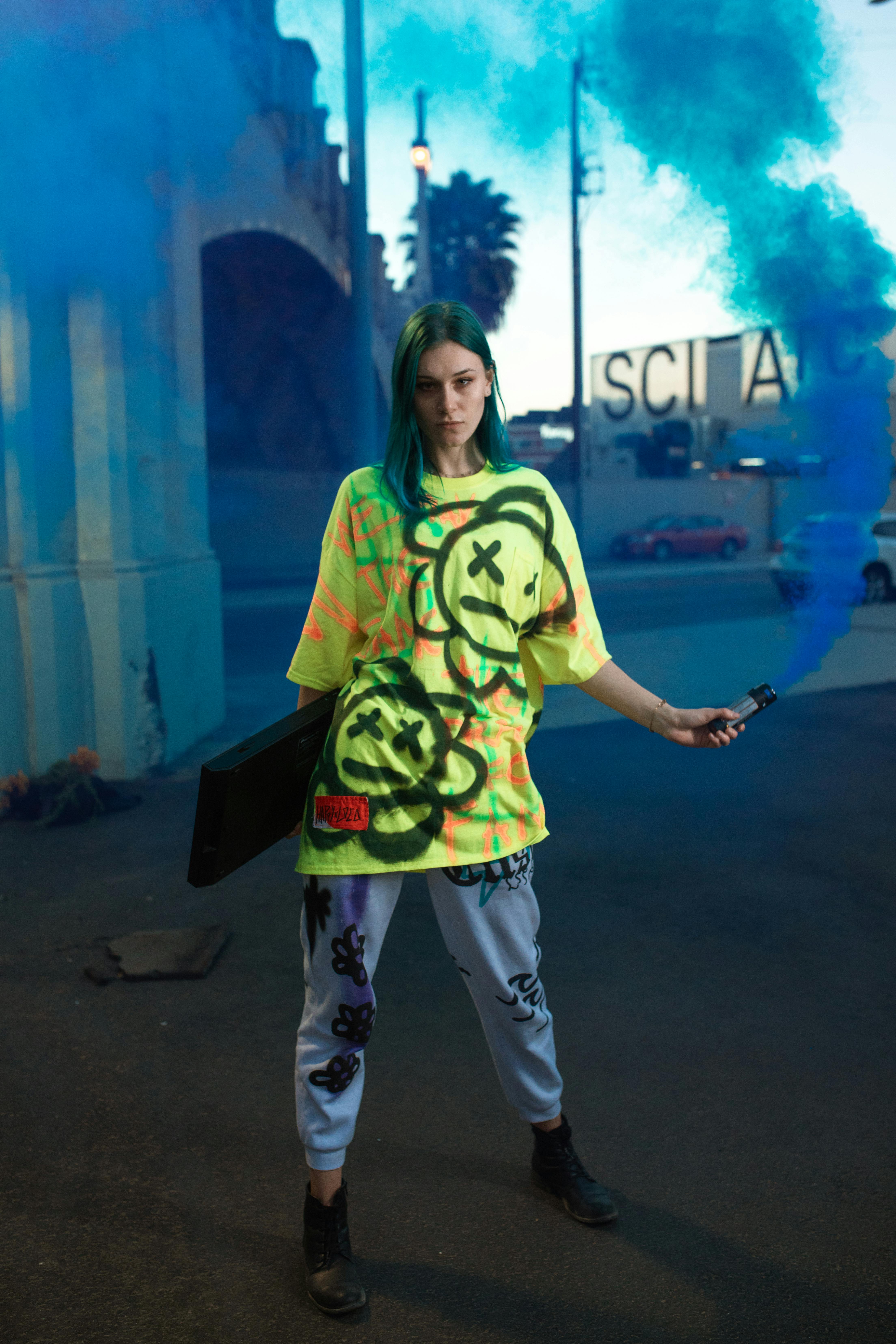 woman in green crew neck t shirt and white pants standing on black asphalt road during