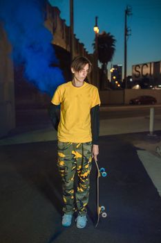 夜色中，穿着鲜艳服装的青少年滑冰运动员手持滑板，滑板上带有蓝色烟雾弹