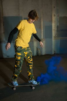 Teen skater boy indoors, performing a skateboard trick with trailing blue smoke for a dramatic effect.