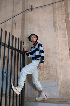 Young adult in striped sweater, climbing urban fence, showcasing modern street fashion.