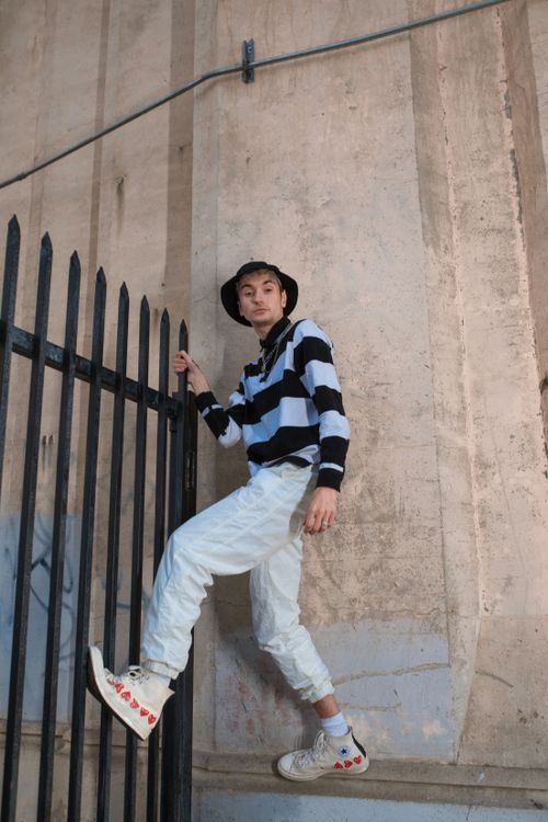 Free Young adult in striped sweater, climbing urban fence, showcasing modern street fashion. Stock Photo