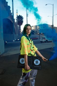 Young woman DJ in neon street style holding a DJ controller with vibrant blue smoke.