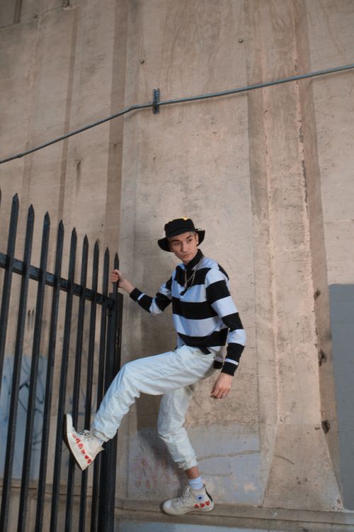 Free Young skater boy in stylish street fashion climbing a fence in the city. Stock Photo