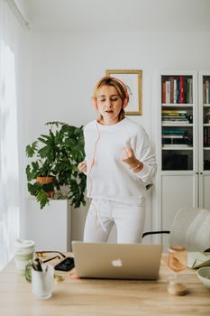 一位女士戴着耳机，在家里的办公桌旁跳舞，享受下班后的休息时光