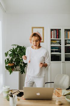 Woman in home office listening to music with headphones, expressing joy and relaxation.