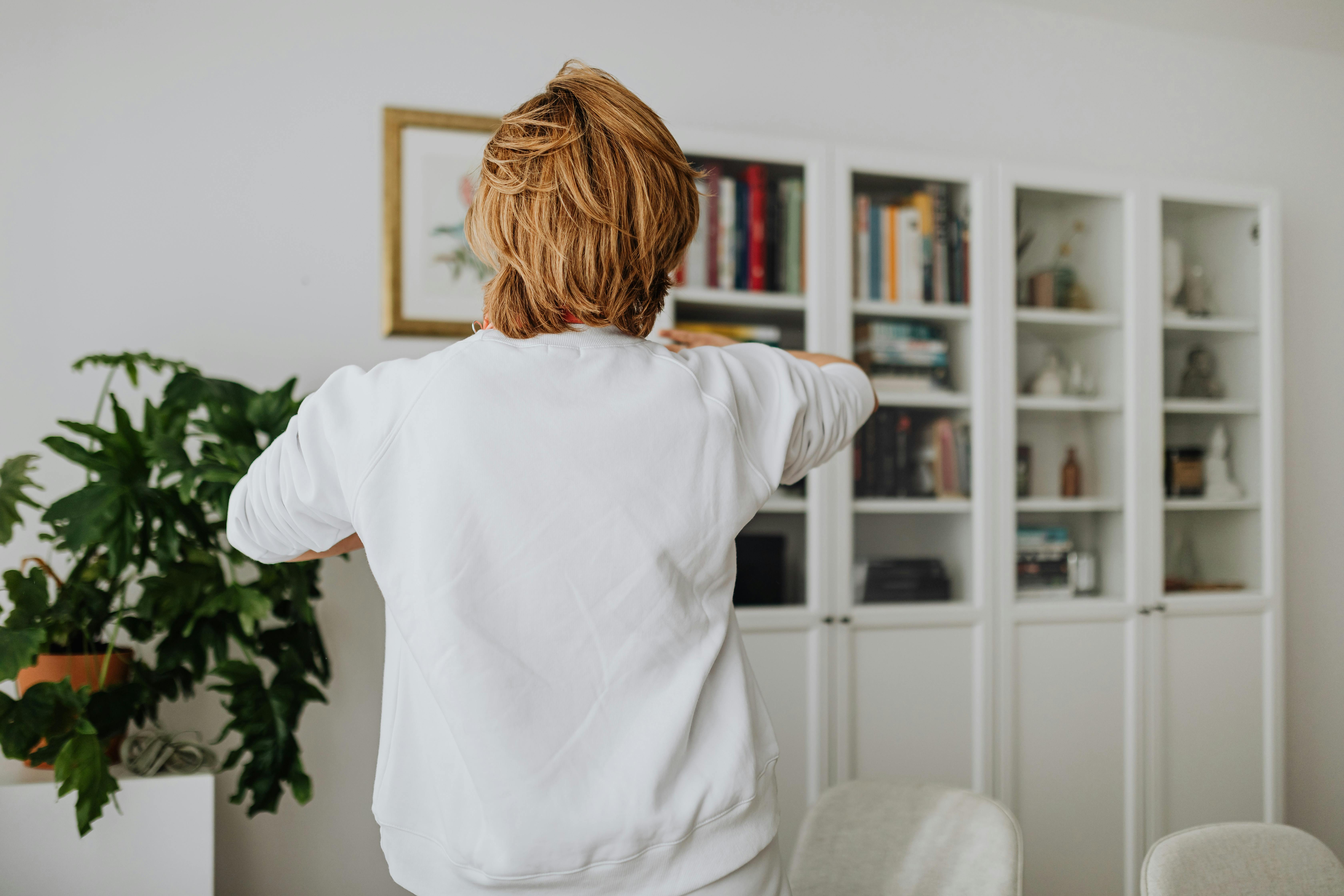 Biała zabudowa biblioteczki w nowoczesnym salonie z równymi półkami i książkami ułożonymi kolorami