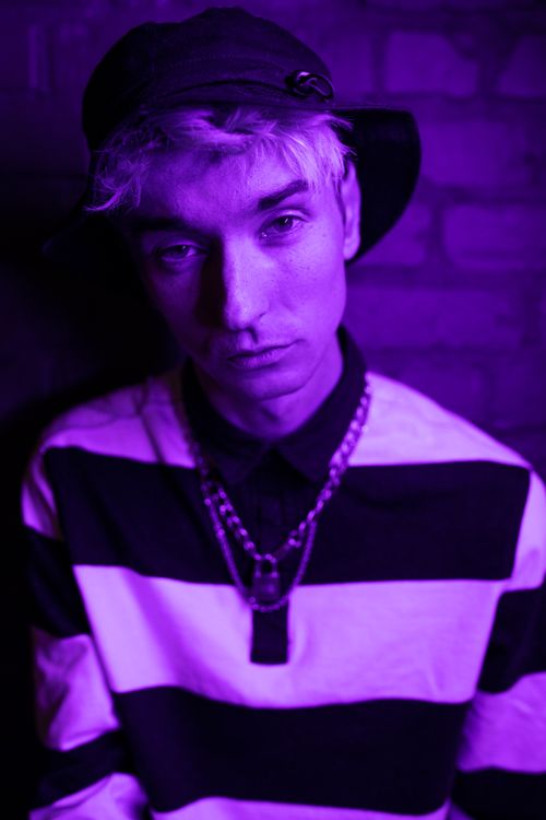 Free Stylish young man posing in vibrant purple neon lighting, showcasing modern fashion aesthetics. Stock Photo