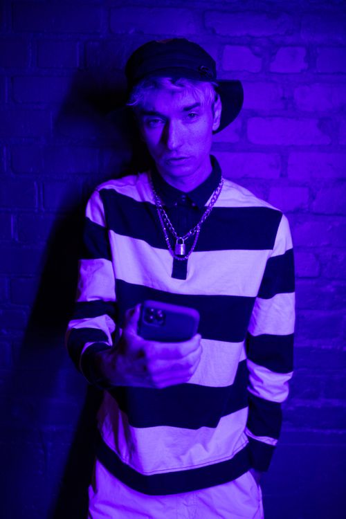 Free A person in stripes using a smartphone against a brick wall under UV light. Stock Photo
