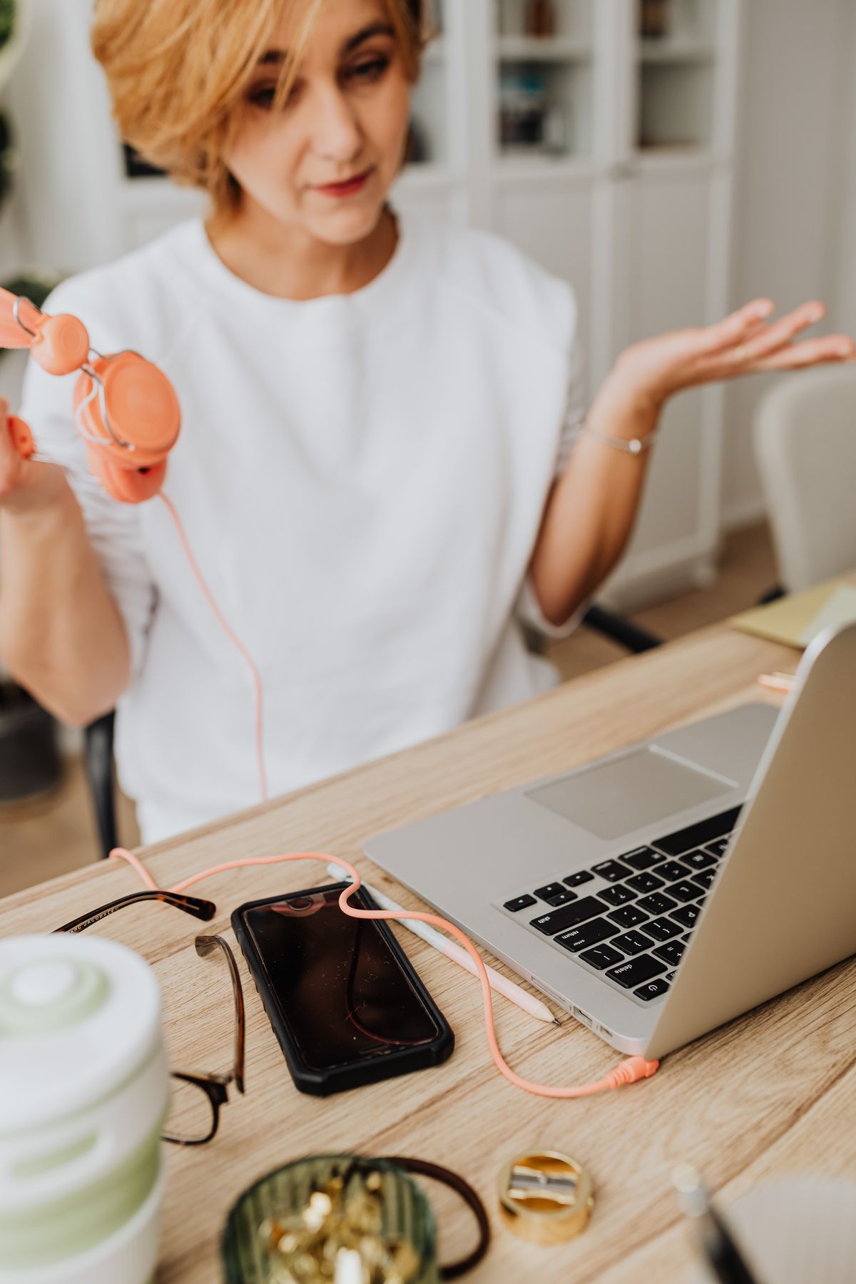 Woman using a laptop, smartphone, and headphones at a home workspace