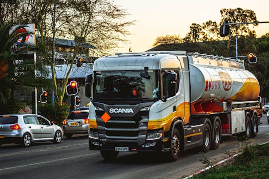 Fuel tanker truck navigating city roads during daytime with traffic signals and surrounding vehicles.