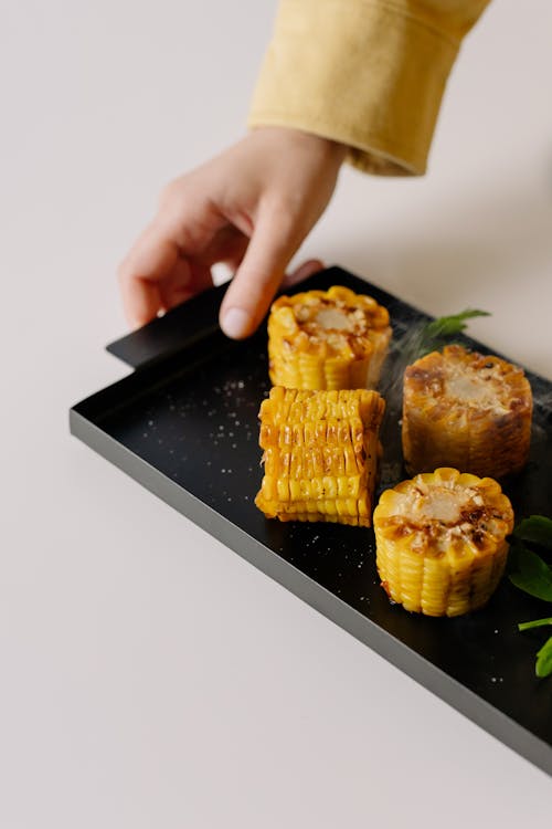 Free Photo of a Person's Hand Holding a Black Serving Tray with Delicious Fried Corn Stock Photo