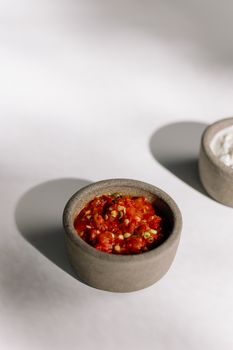 白色桌子上石碗中辛辣红辣椒蘸香料的特写，非常适合美食爱好者