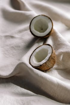 Coconut halves resting on soft white cloth, showcasing a minimalist still life composition.
