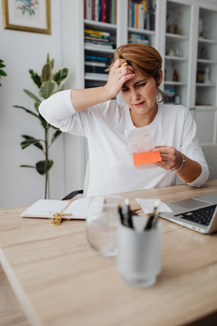 Woman At Desk Looking At Receipt And Scratching Her Head