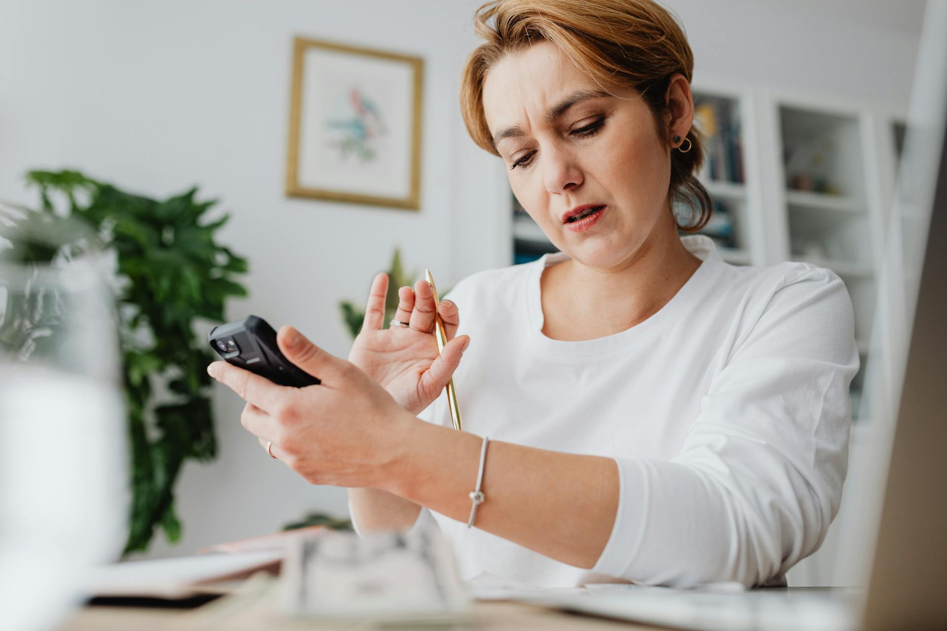 A woman intensely focuses on a calculator while managing work from a home office setup.