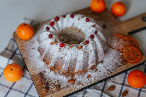 Free A powdered sugar-topped Bundt cake with almonds and citrus fruit garnishing on a wooden tray. Stock Photo