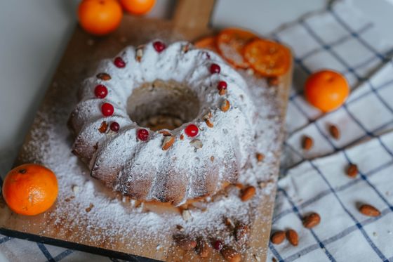 Bundt cake dusted with powdered sugar, topped with cranberries and almonds, surrounded by clementines