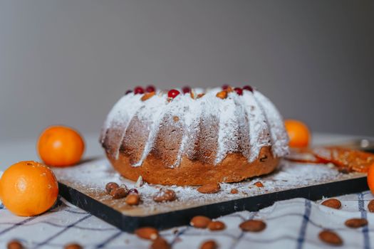 Close-up of a powdered Bundt cake with oranges and almonds on a tray.