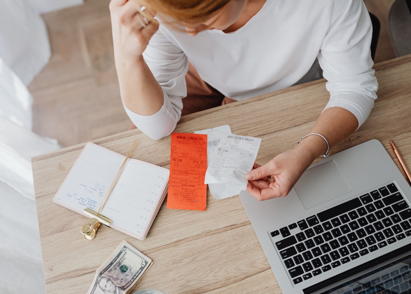 A person sorting receipts and planning a monthly budget on a laptop at home