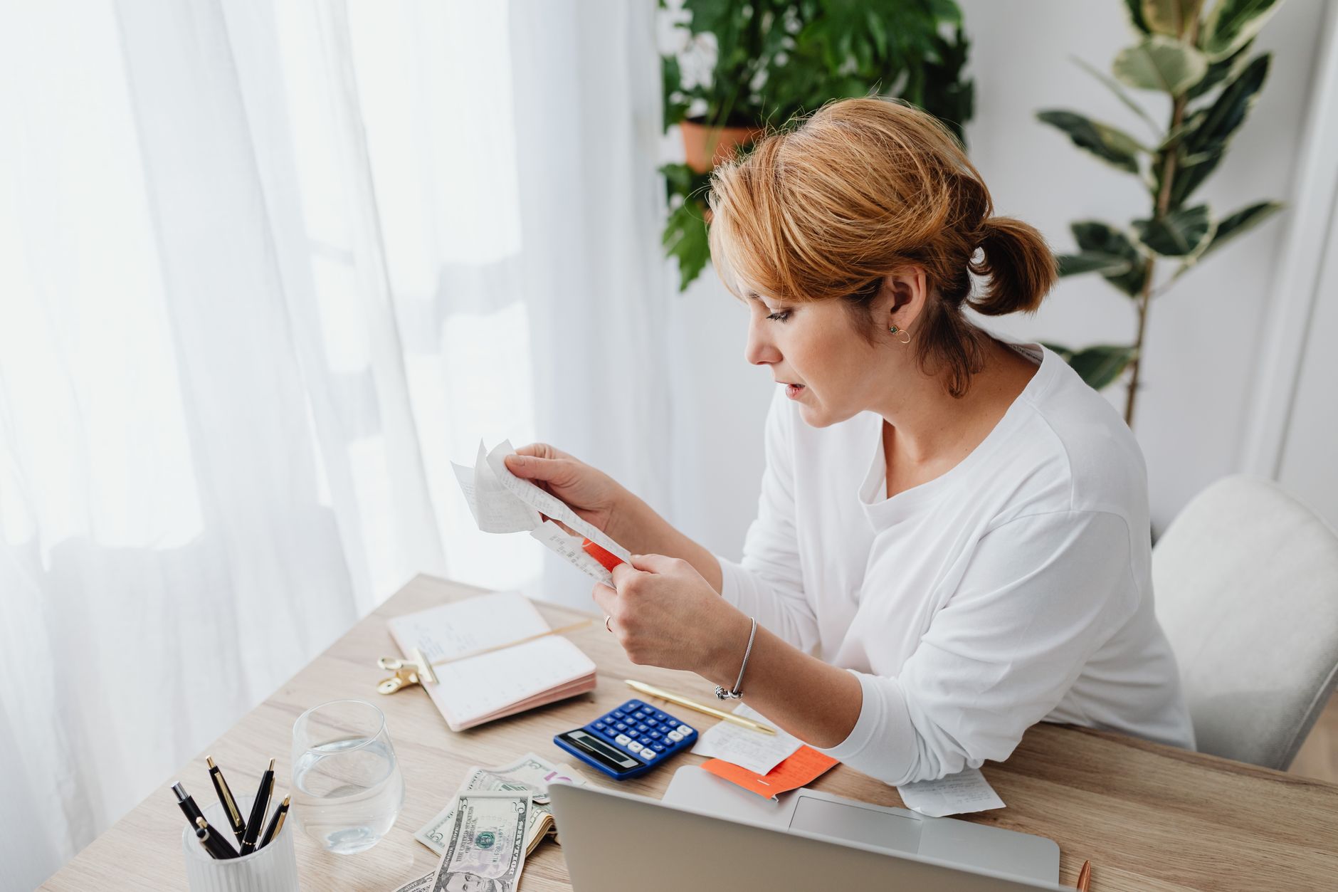 Woman sitting at a desk managing finances with a calculator and paper receipts in an office setting.