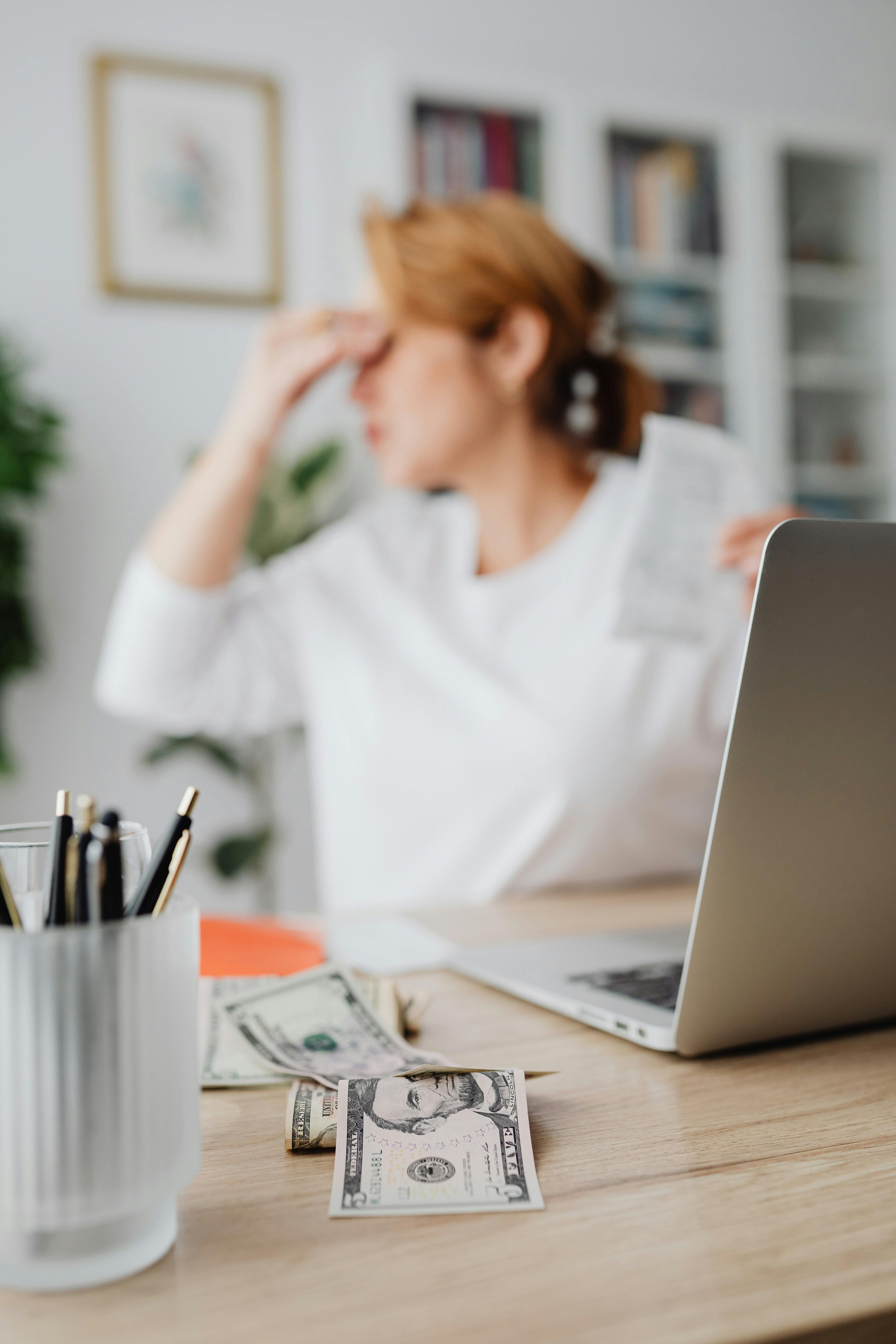 dollar bills and laptop on desk and woman distraught in background