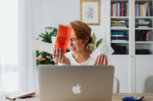 Free Frustrated woman managing finances, surrounded by bills and a laptop, looking distressed. Stock Photo