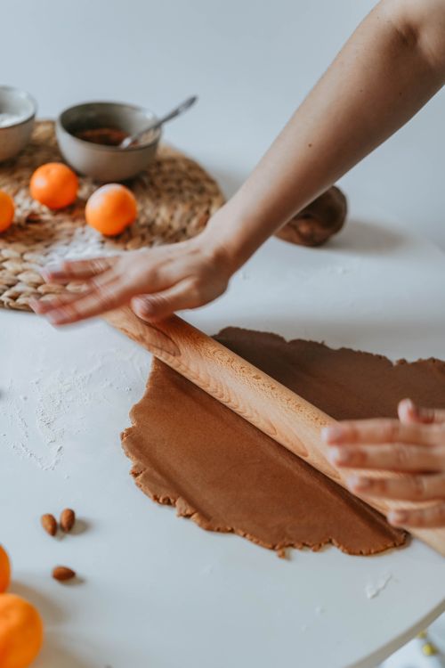 Free Hands kneading dough with a rolling pin on a white table surrounded by fruits and kitchen items. Stock Photo