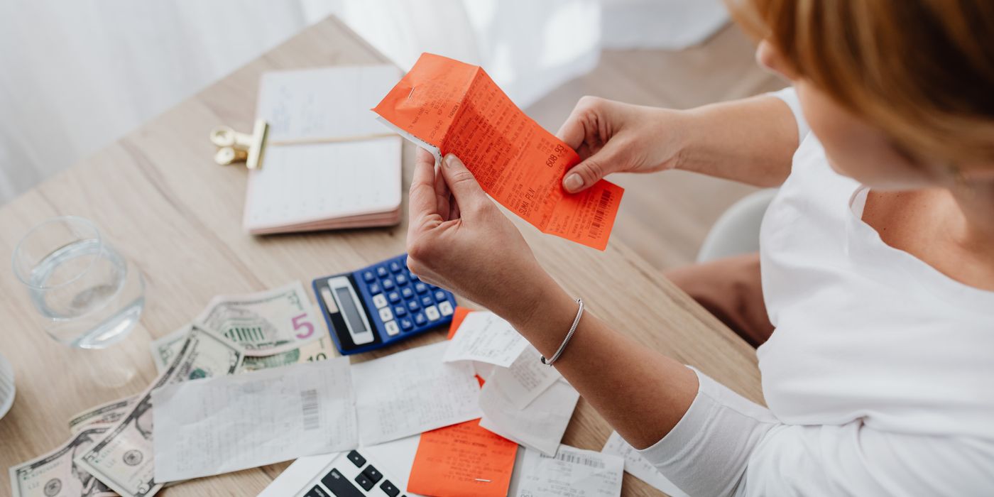 Woman using calculator and receipts at home office desk for finance management.