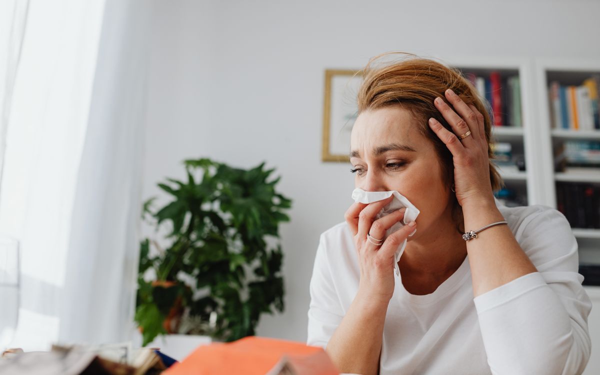 An adult woman feeling unwell, blowing her nose indoors.