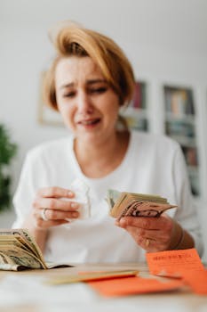 Woman emotionally managing finances at home, counting money and reviewing bills.