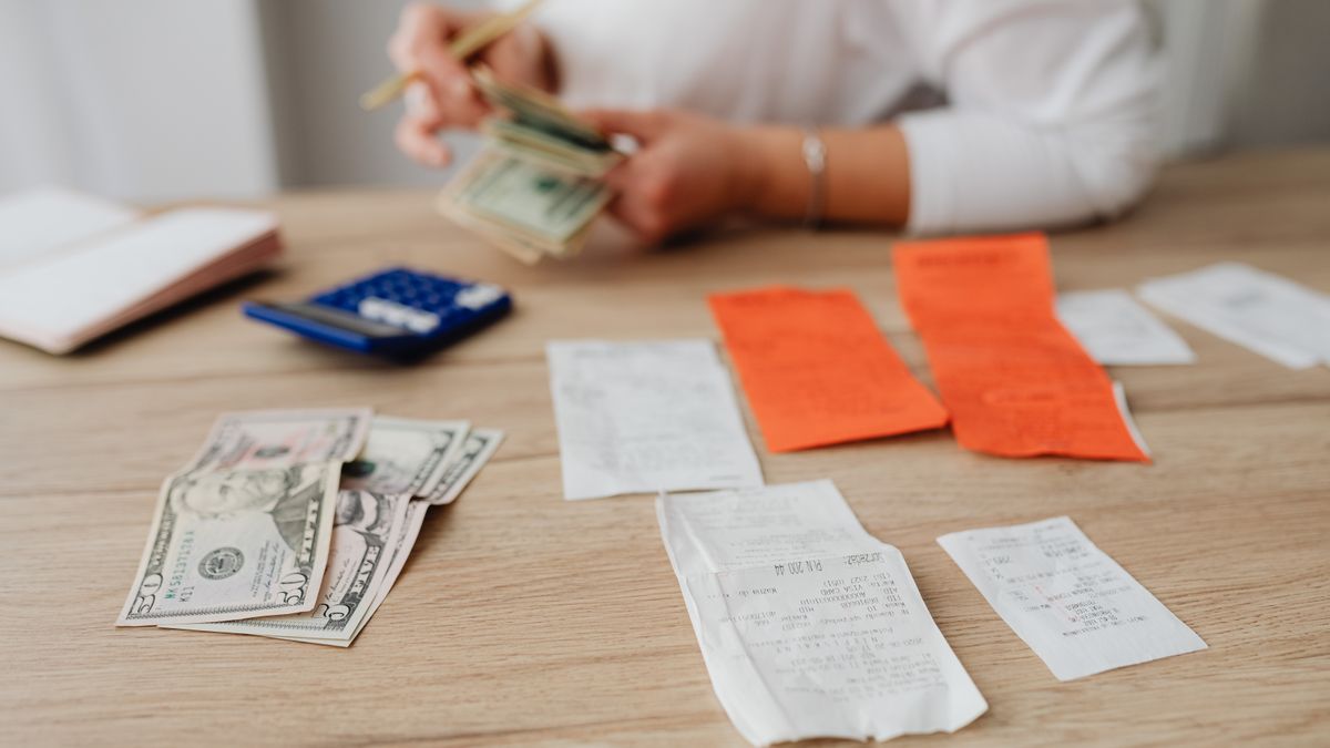 A person using a calculator and cash to plan a household budget.