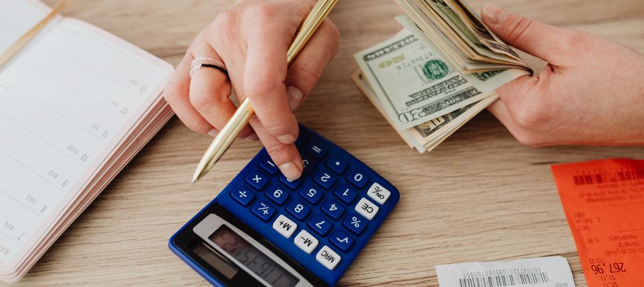 Hands working out a household budget with cash and a calculator — weighing up pest control prices in Malaysia